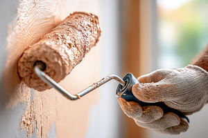 Hand applying paint with roller on wall in a room during daylight hours, an Industrial Photo by AlyaAnd