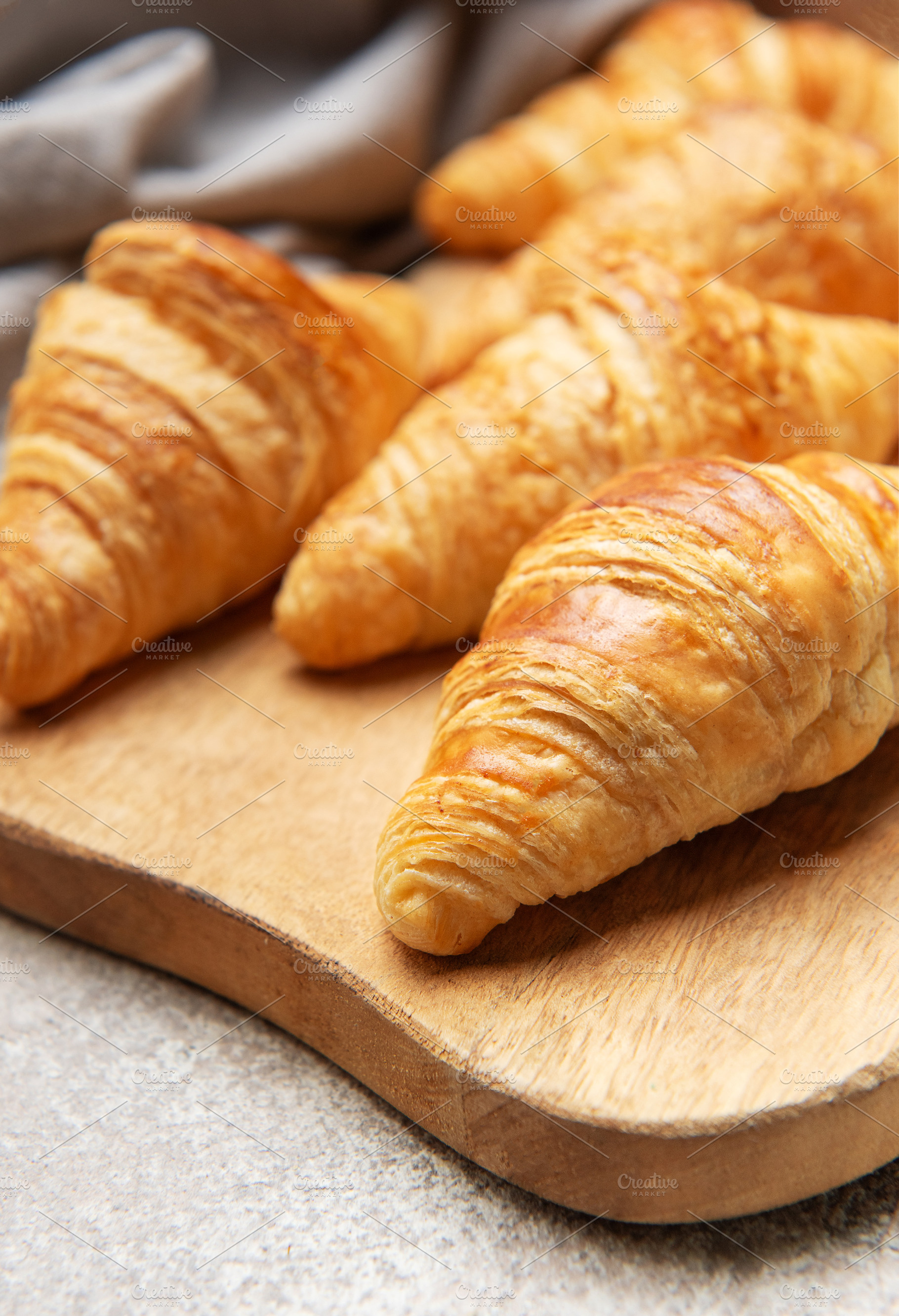 Freshly baked croissants resting on wooden cutting board, a Food & Drink Photo by Olena Rudo