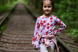 Young girl posing confidently in a scenic forest trail with railway tracks, a Photo by AS photostudio