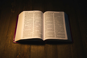 Open Holy Bible over a wooden table