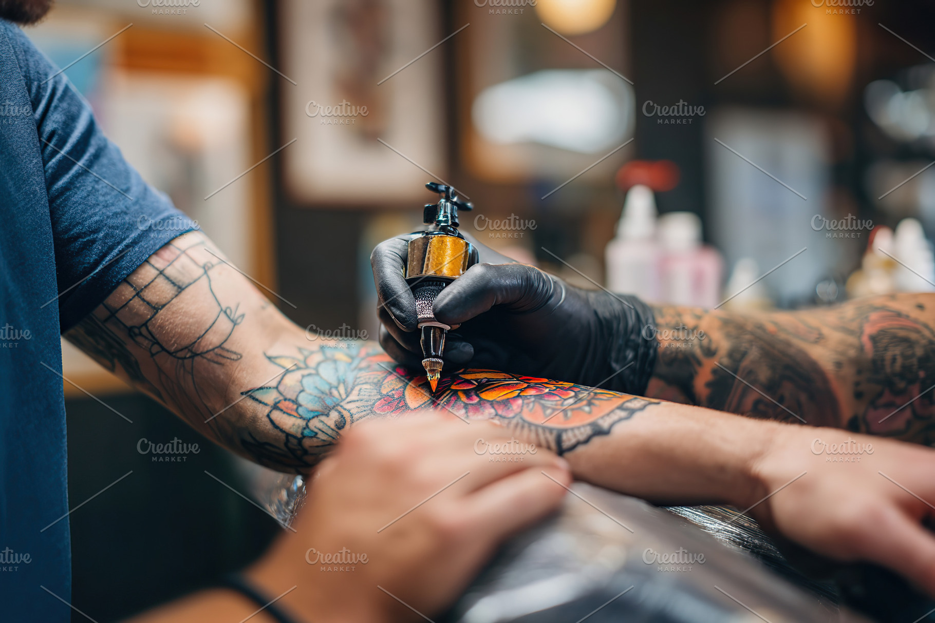 Artist inking a colorful flower design on a tattoo client's arm in a busy studi, an Arts & Entertainment Photo by AlyaAnd