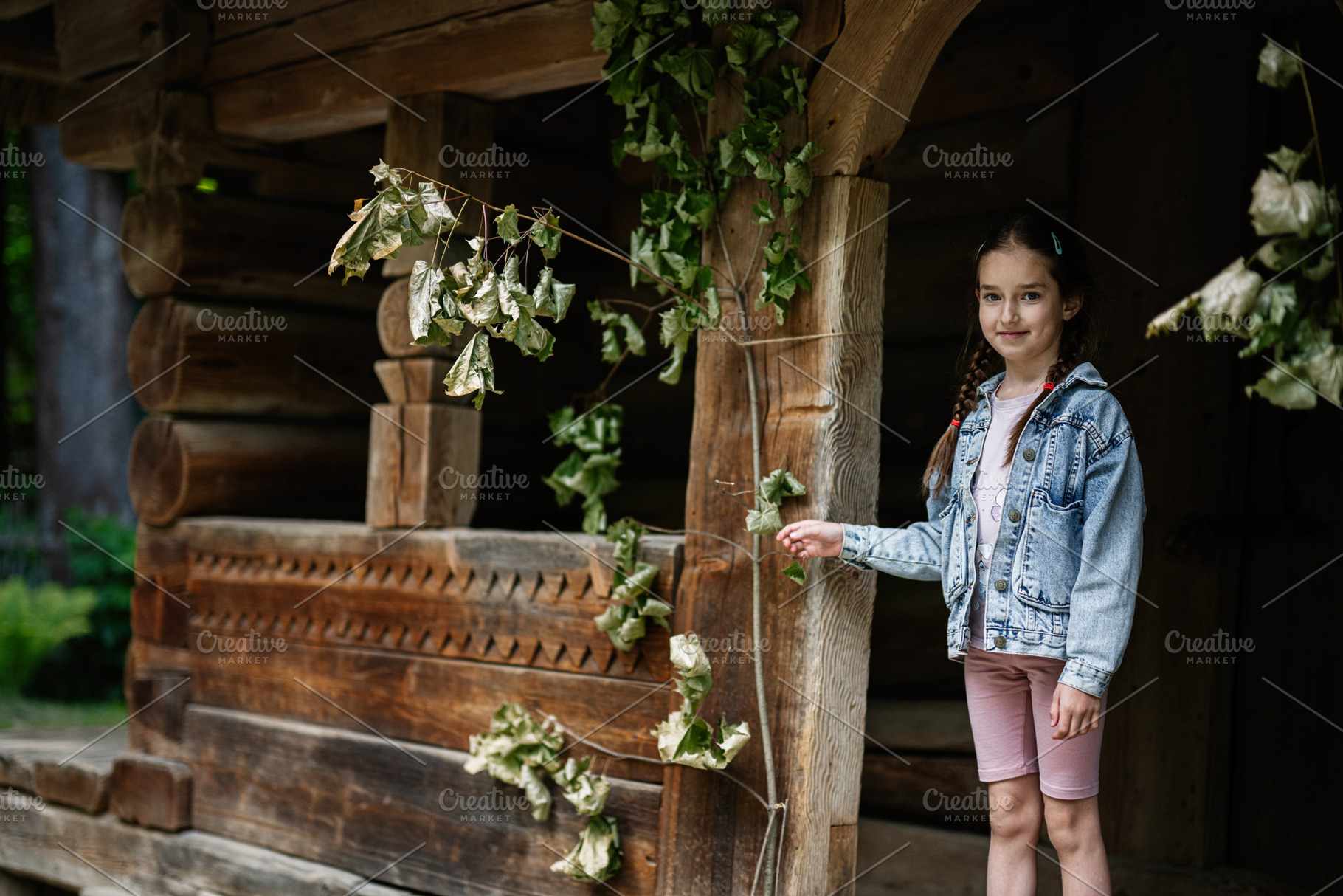 Young girl standing by traditional wooden structure surrounded by foliage outdo, a Person Photo by AS photostudio