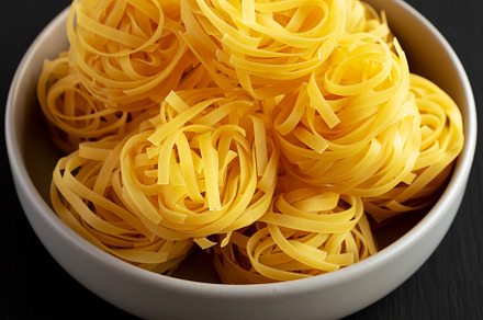 Raw Dry Tagliatelle Pasta in a Bowl, side view., a Food & Drink Photo by LiudmylaChuhunova