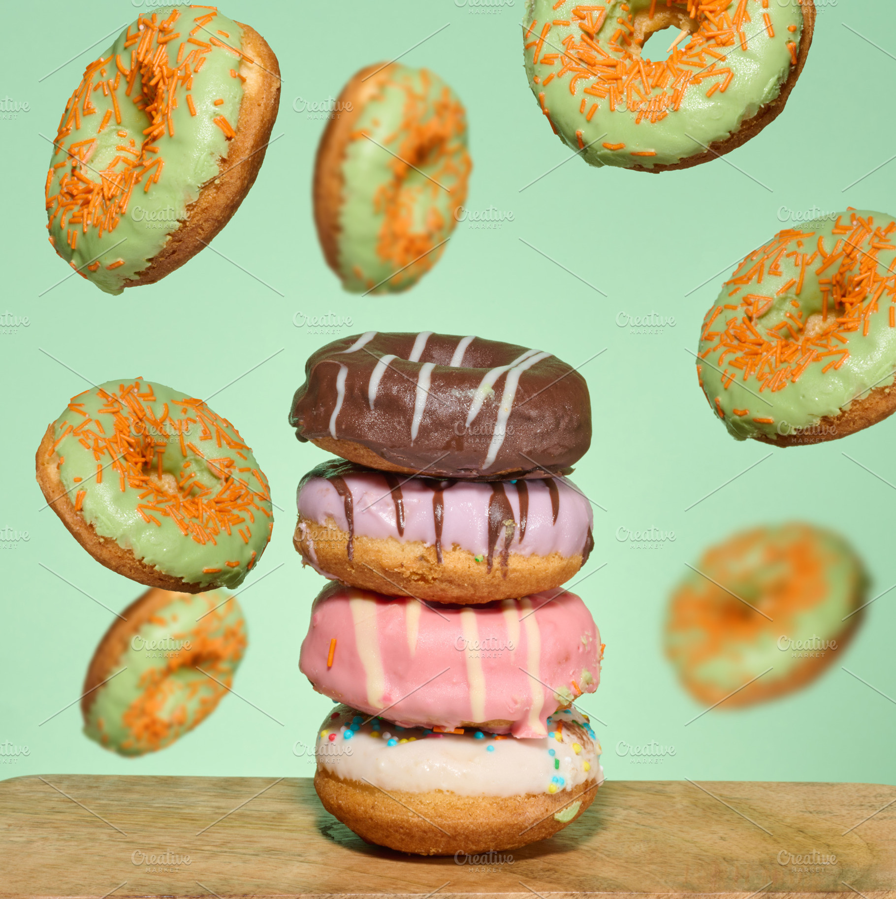 A stack of four brightly glazed donuts on a table with green don, a Food & Drink Photo by ndanko
