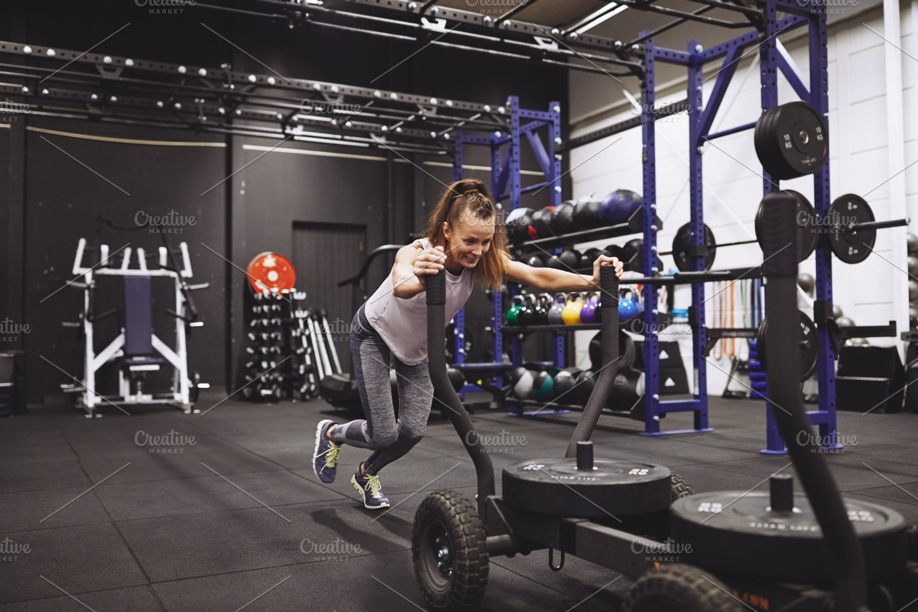 Smiling mature woman pushing a sled during a gym workout, a Sports & Recreation Photo by Stefan & Janni