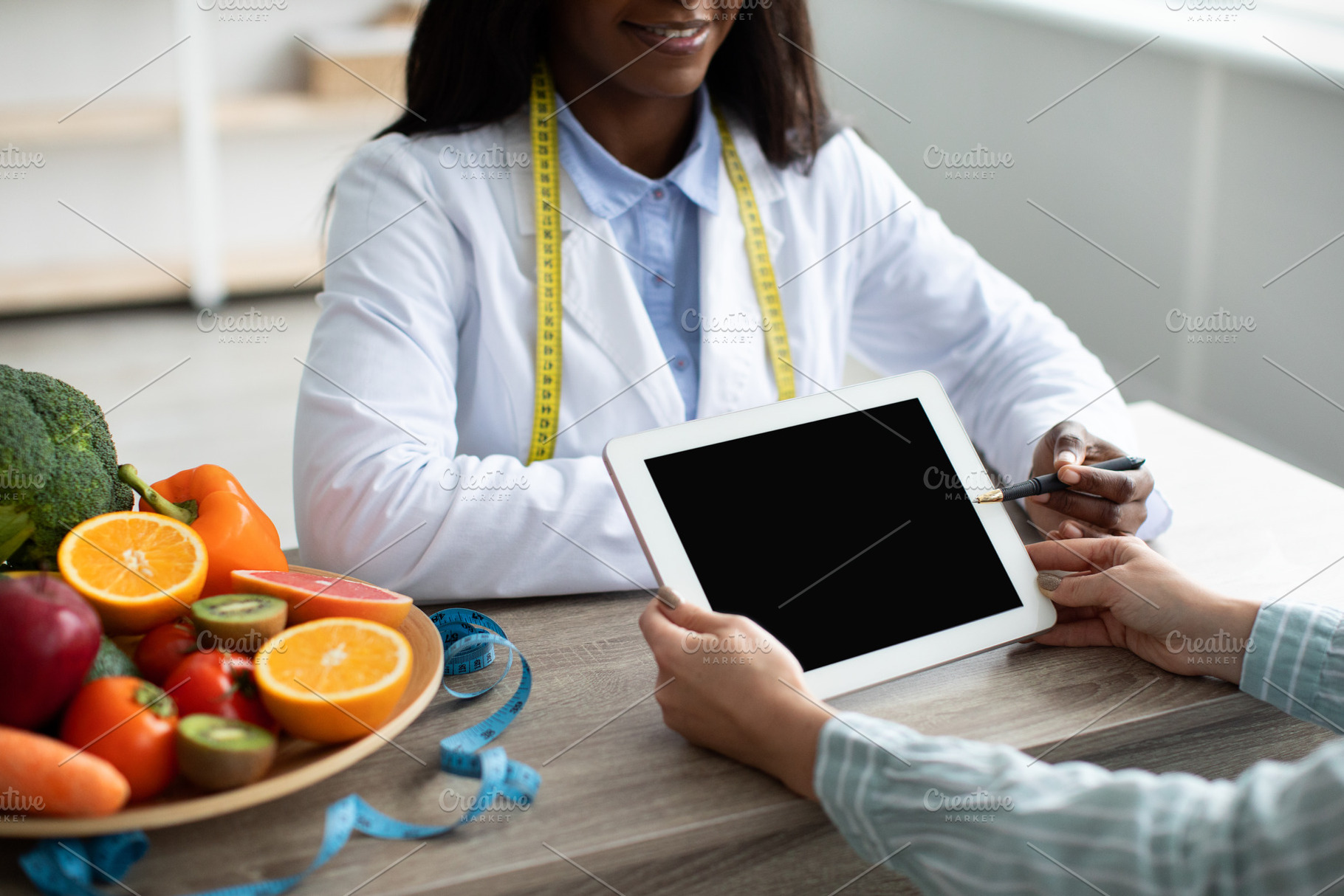 Black female dietitian pointing at tablet with blank screen, explaining diet pl, a Person Photo by Prostock-Studio