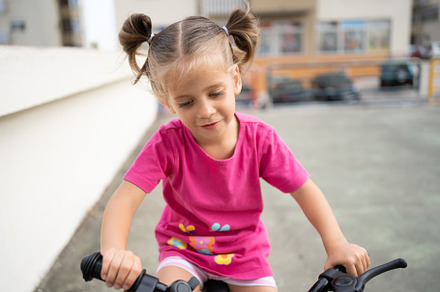Cute little smiling girl riding bike bicycle in city on parking sunny summer da, a Person Photo by andreonegin market