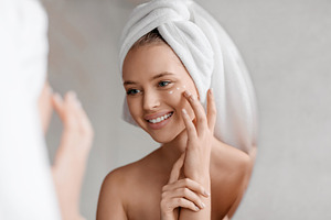 Portrait of young lady applying nourishing eye cream after shower, looking at m, a Photo by Prostock-Studio