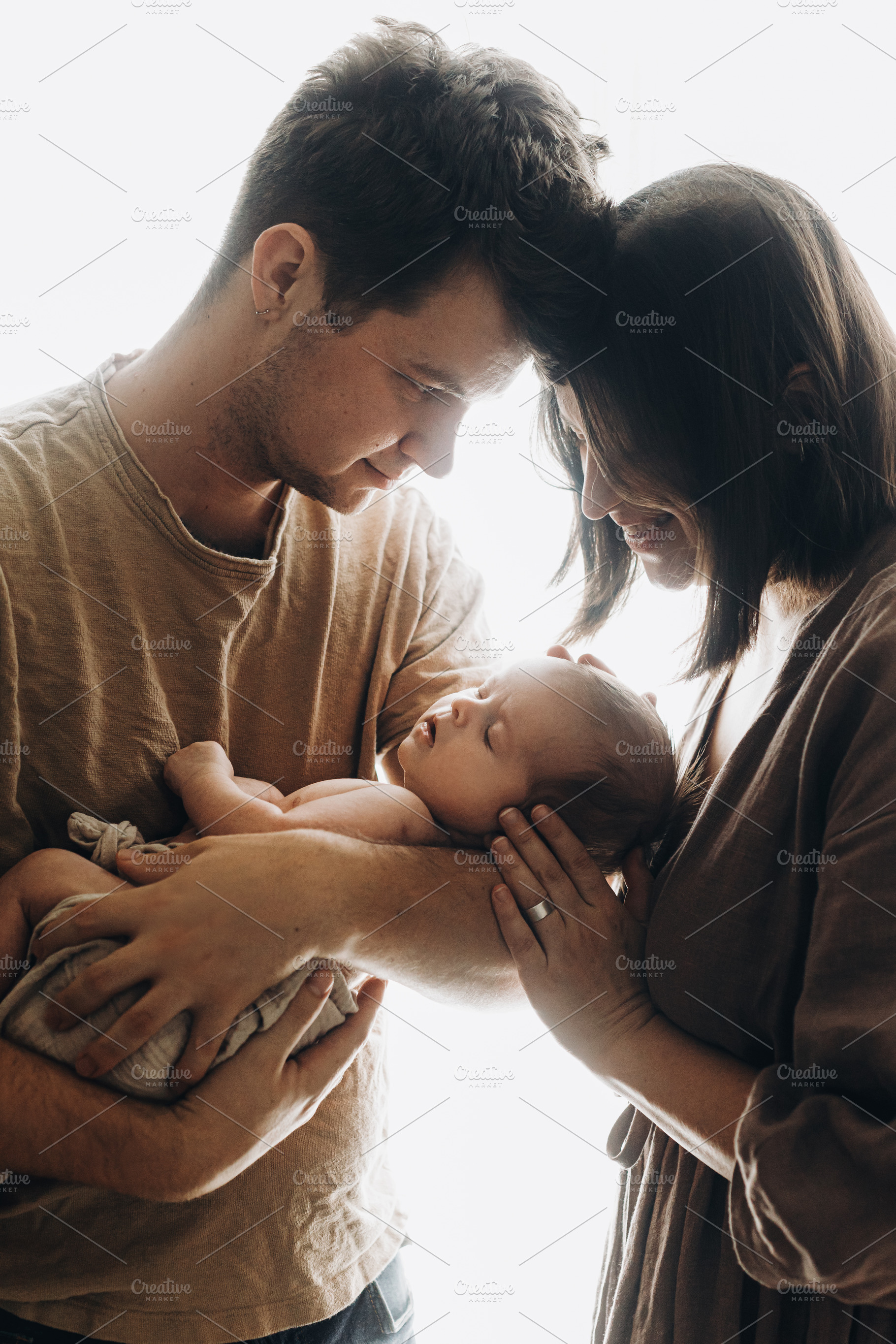 Happy mother and father hugging little baby son in window light., a Person Photo by Sonjachni