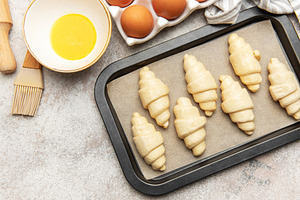 Baker preparing raw croissants on baking tray for baking, a Food & Drink Photo by Olena Rudo