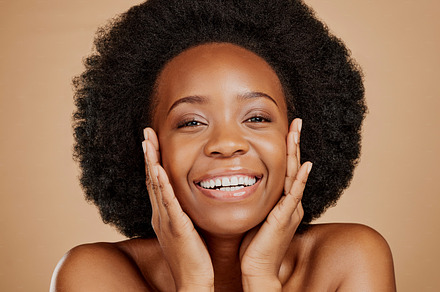 Portrait, happy black woman and touch face for skincare, aesthetic glow and soft dermatology on brown background. Female model, natural beauty and afro hair in studio for shine, facial and self care, a Photo by Peopleimages.com