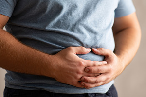 Man holding his stomach in pain abdo, a Photo by Pixeness Studio