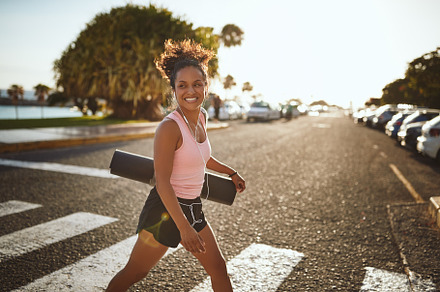 Sporty woman smiling enthusiastically while walking to yoga clas