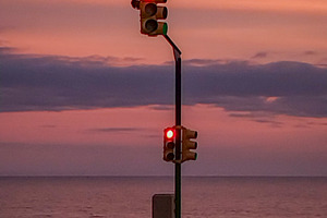 Traffic light glowing at sunset by the sea, a Transportation Photo by DanFLCreativo