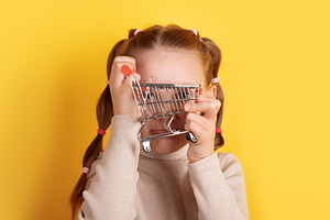 Young girl holding a small shopping cart in front of her face ag, a Person Photo by Ales Munt