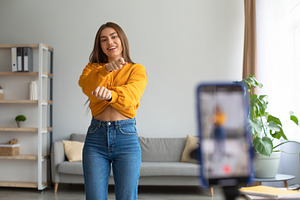 Young Caucasian female influencer recording video on smartphone, dancing on cam, a Photo by Prostock-Studio