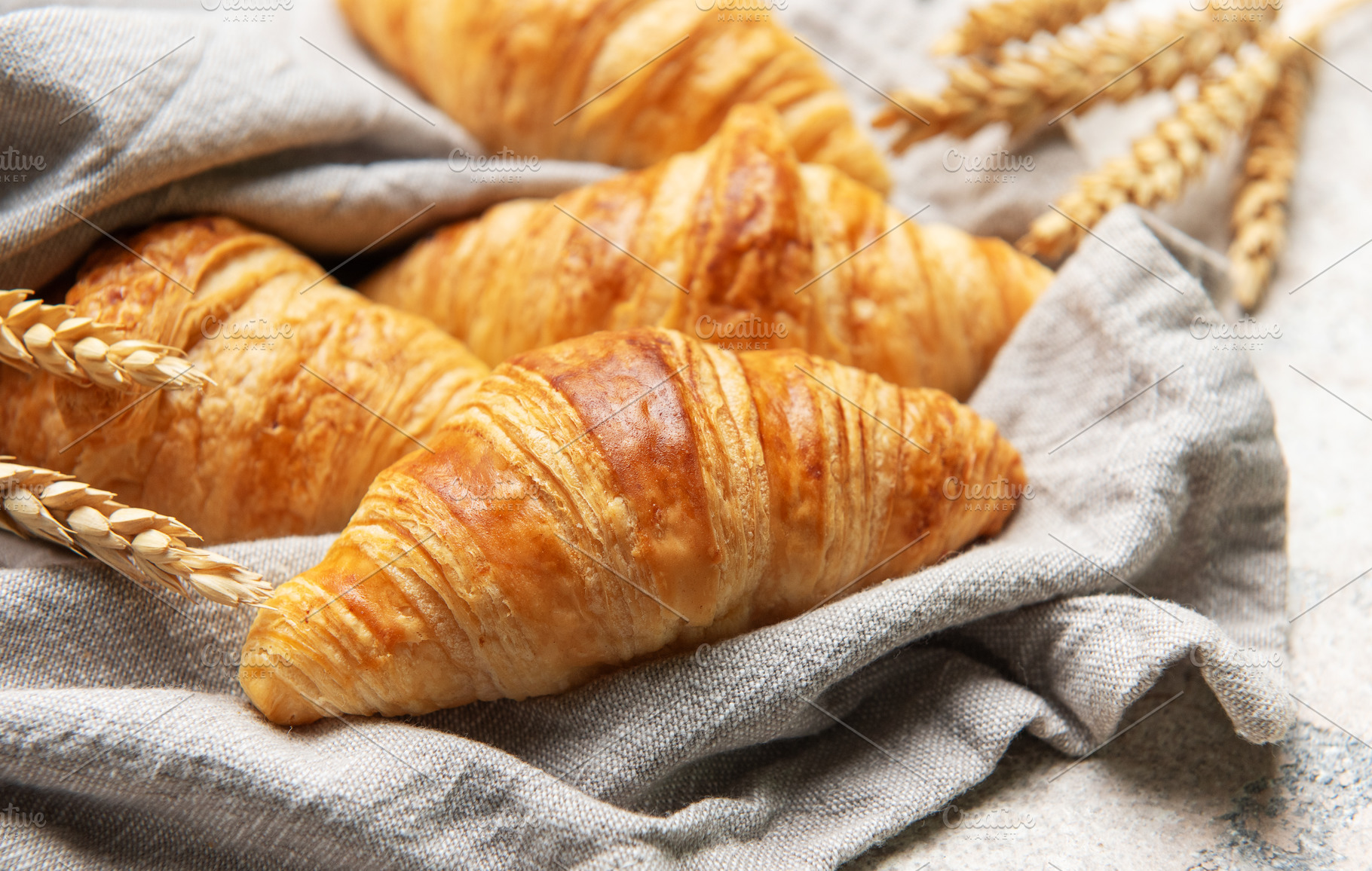 Freshly baked croissants resting on a linen cloth with wheat sta, a Food & Drink Photo by Olena Rudo