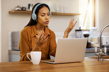 Young serious mixed race businesswoman talking while on a virtual meeting using a laptop at home. One hispanic female businessperson talking and wearing headphones while on a call using a laptop, a Photo by Peopleimages.com