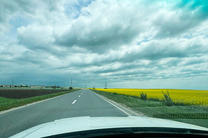 Scenic rural road with a vibrant yellow field under a blue cloudy sky, a Photo by AS photostudio