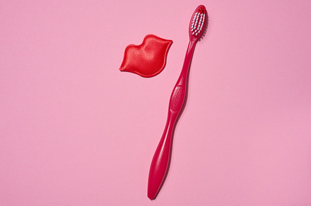 Red toothbrush and red decorative lips placed on a pink backgrou