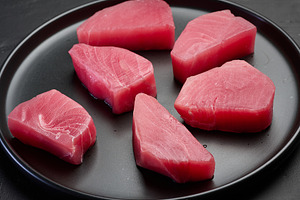 Raw tuna pieces on a black round plate, top view, a Food & Drink Photo by ndanko