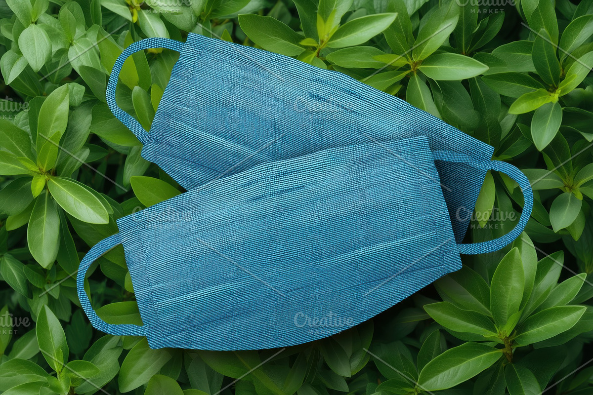 Two blue medical masks mockup placed on a bed of green leaves, a Mask Mockup by Textures & Backgrounds