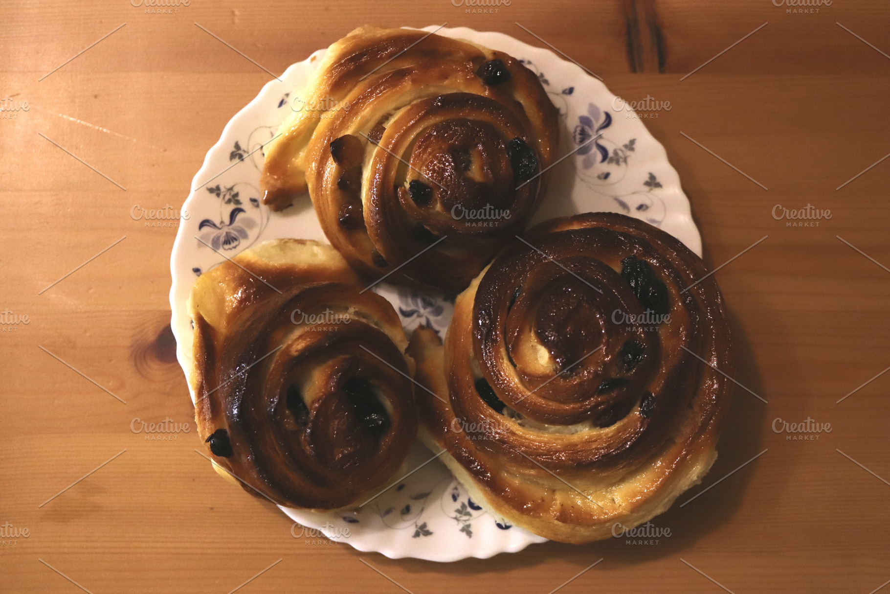 Three cinnamon rolls with raisins on a floral plate, a Food & Drink Photo by Textures & Backgrounds
