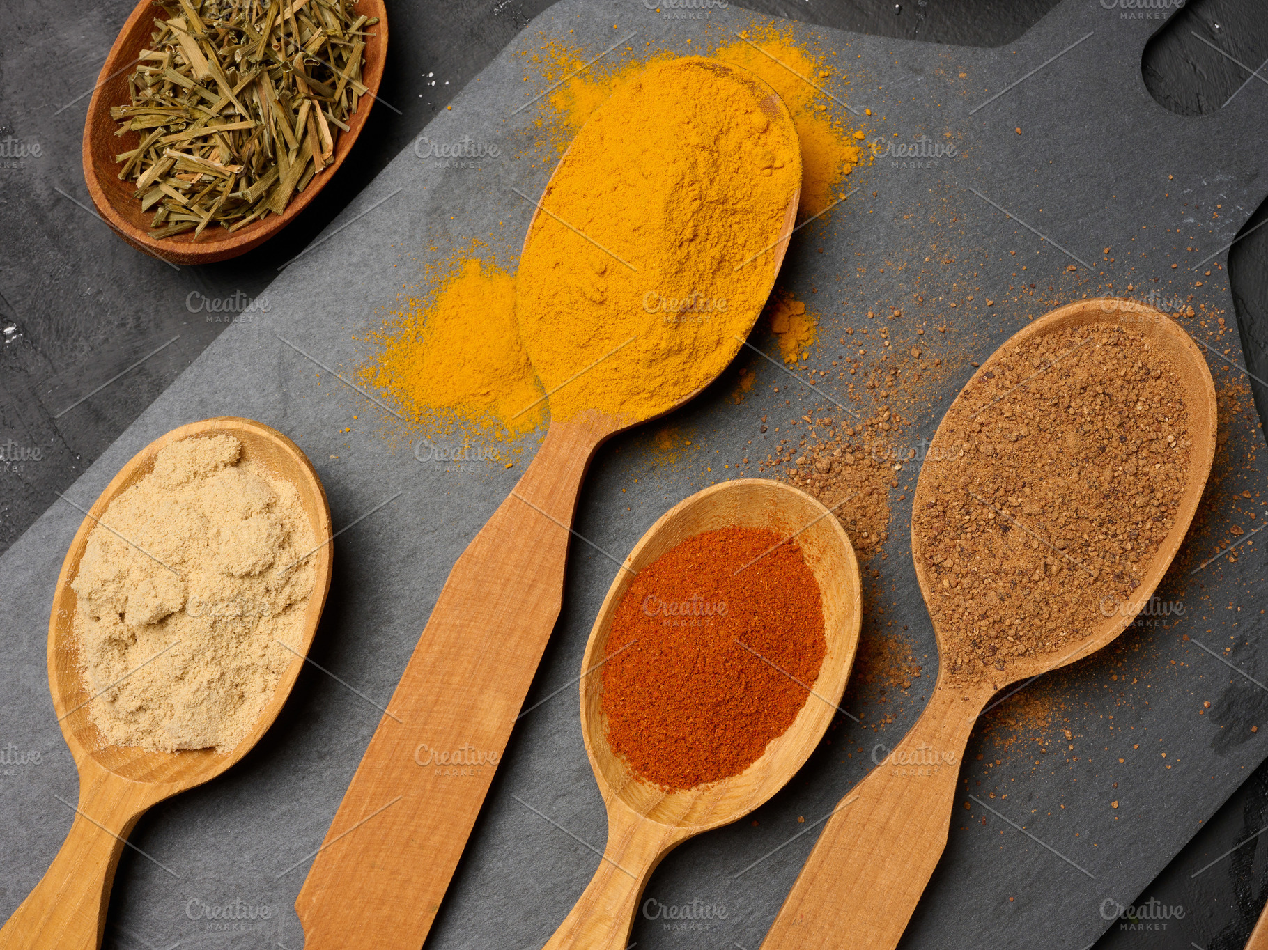 Assorted ground spices in wooden spoons, turmeric, paprika, nutm, a Food & Drink Photo by ndanko