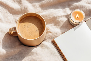 Ceramic coffee cup on soft fabric with a candle and an open notebook in morning, a Food & Drink Photo by AlyaAnd
