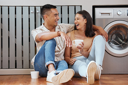Happy, carefree and romantic couple bonding, laughing and having fun while sitting on the floor. Loving cheerful husband and wife having a cup of coffee, talking and relaxing in the kitchen at home, a Photo by Peopleimages.com