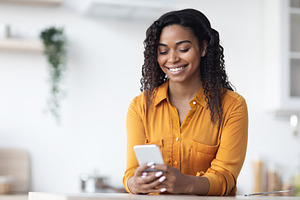 Cheerful black woman using brand new smartphone at home