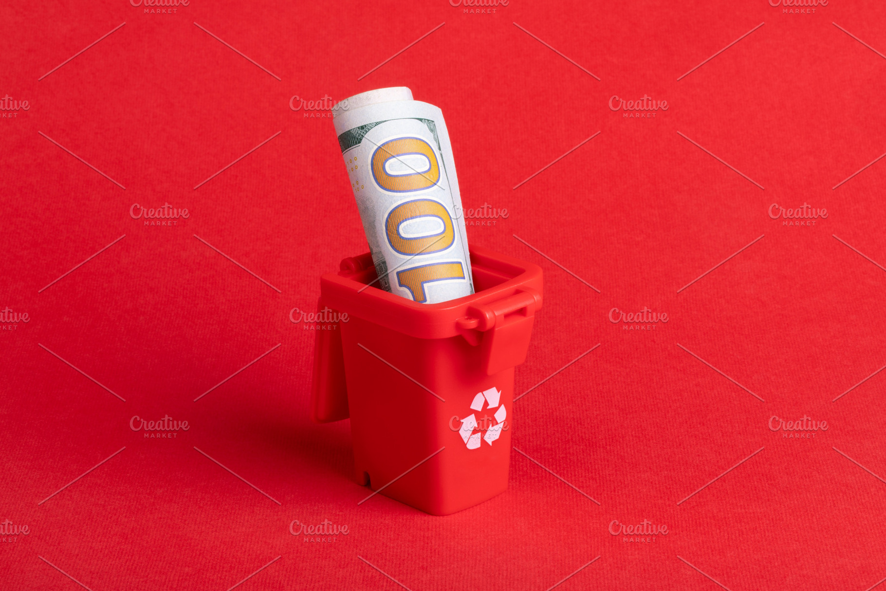 Rolled hundred dollar bill placed in a small red recycling bin on a solid red b, a Business Photo by Ales Munt