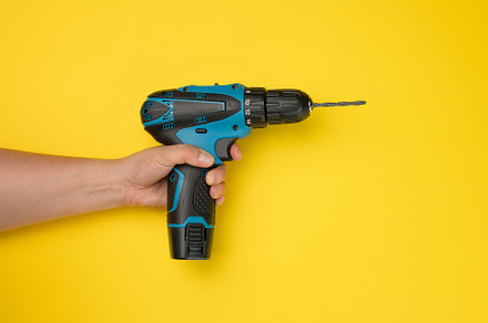 female hand holds a cordless drill on a yellow background. Tool, an Abstract Photo by ndanko