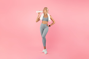 Sporty woman drinking water from bottle after exercising, a Photo by Prostock-Studio