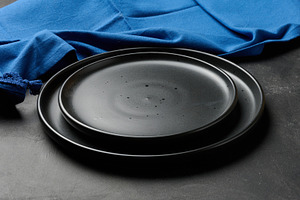 Empty black ceramic plates stacked on dark background with blue, a Food & Drink Photo by ndanko