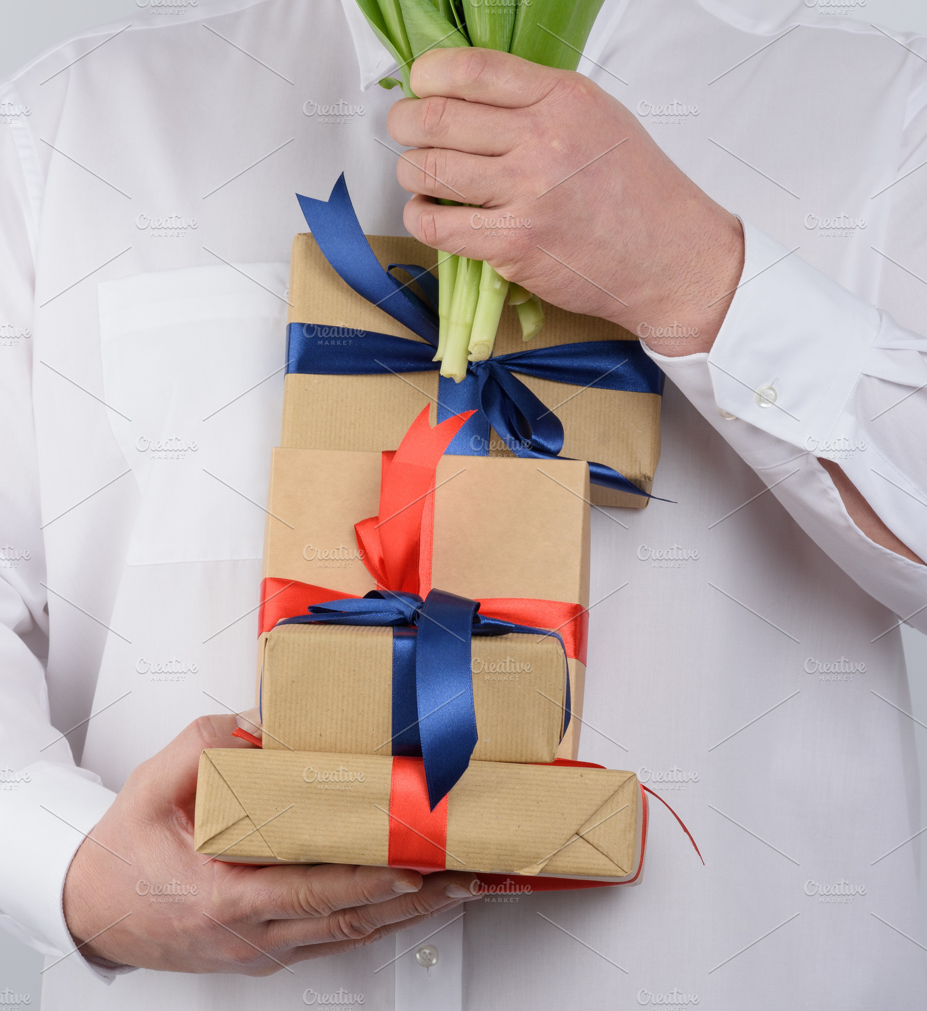 A man in a white shirt holds a stack of craft-wrapped gifts tied, a Person Photo by ndanko