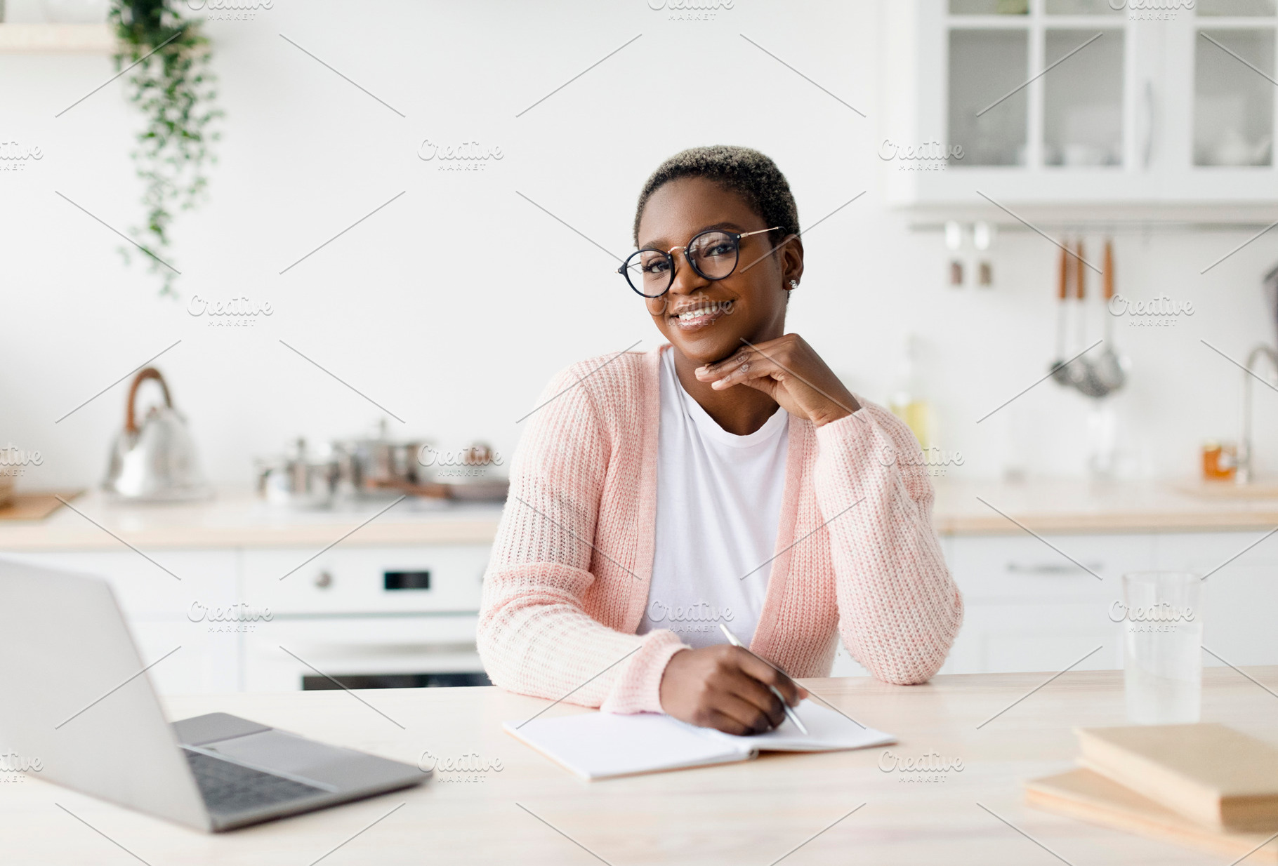 Happy young black lady in glasses and casual sits at table looks at laptop make, a Person Photo by Prostock-Studio