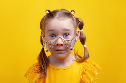 Wide-eyed girl in yellow dress wearing dangling rhinestone glass