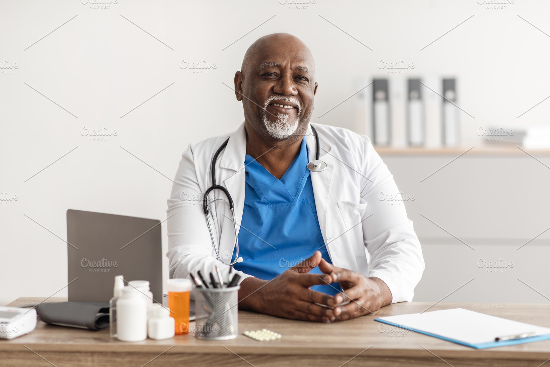 Portrait of smiling doctor looking at camera sitting at desk, a Photo by Prostock-Studio