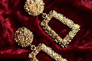 Golden textured dangle earrings showcasing luxury and glamour on a rich red vel, a Photo by Studio ANNA