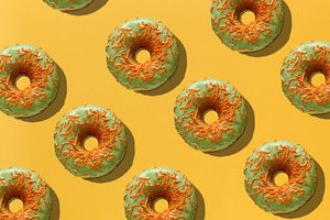 Green donuts with orange sugar sprinkles on yellow background, t, a Food & Drink Photo by ndanko