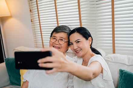 Asian mom and daughter taking selfie on sofa