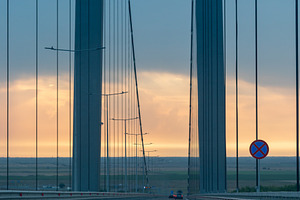 Wide view of a modern suspension bridge at sunset with cars crossing, dramatic, an Architecture Photo by Ales Munt