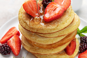 Pouring syrup over homemade pancakes with fresh berries, a Food & Drink Photo by Olena Rudo