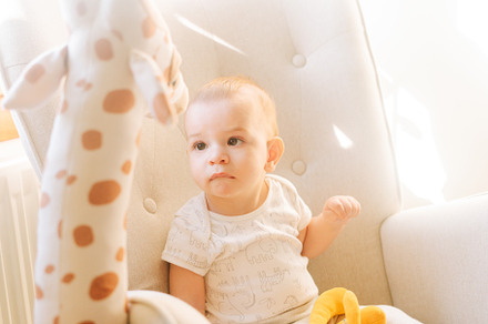 Portrait of a nine month old baby with a stuffed giraffe sitting in a rocking c