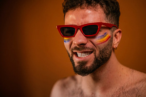Man in red sunglasses with rainbow face paint celebrating, a Photo by karrastock