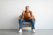 Portrait of mature man using smartphone sitting on armchair, a Photo by Prostock-Studio (Thumbnail 1 of 2)