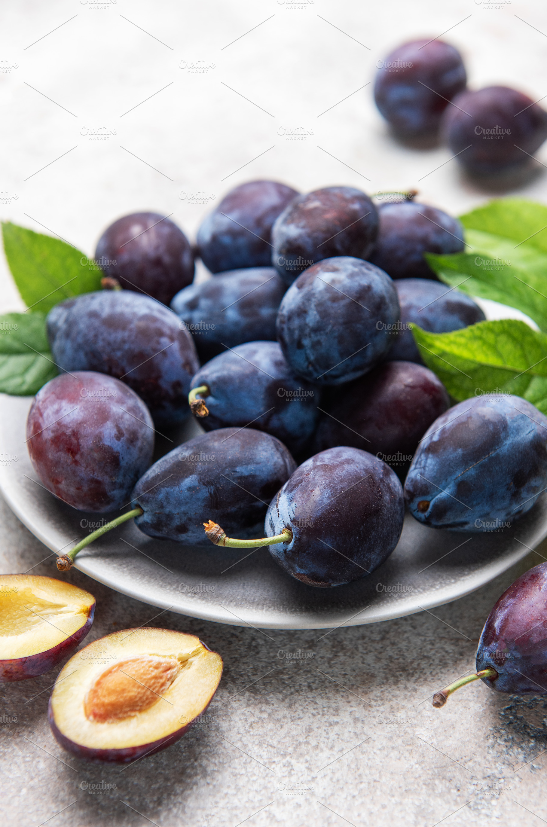 Fresh ripe plums, whole and halved on plate, a Food & Drink Photo by Olena Rudo