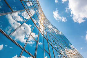 Building facade reflects clouds in clear blue sky during sunny daylight hours, an Architecture Photo by AlyaAnd