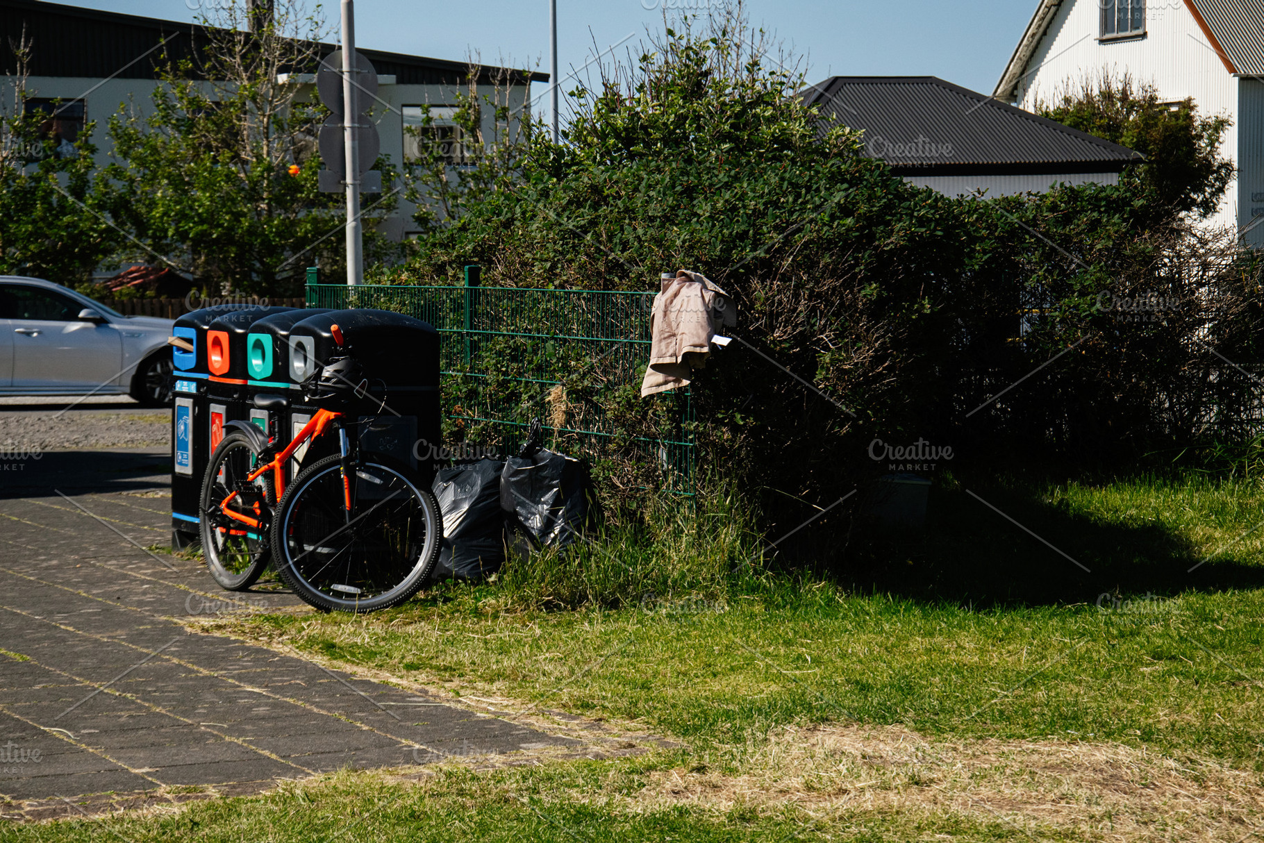 Orange bicycle beside bins and greenery on a sunny day in Akranes, Iceland, a Photo by AS photostudio